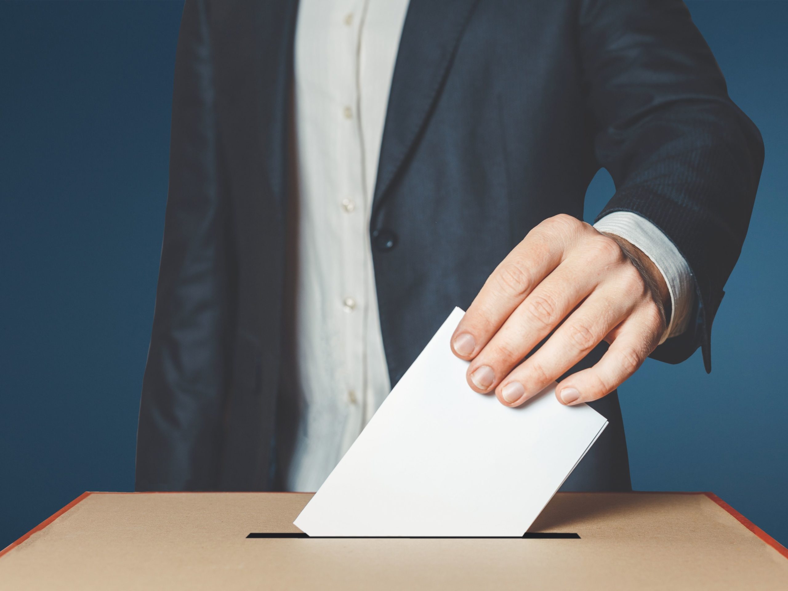 a mão de um homem a meter um boletim de voto numa urna