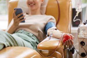 mulhersentada numa cadeira a mexer no telemóvel enquanto doa sangue
