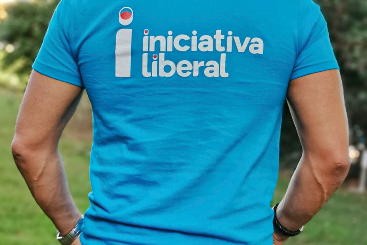Uma homem, de costas, vestido com uma t-shirt azul onde está escrito, em letras brancas, iniciativa liberal.